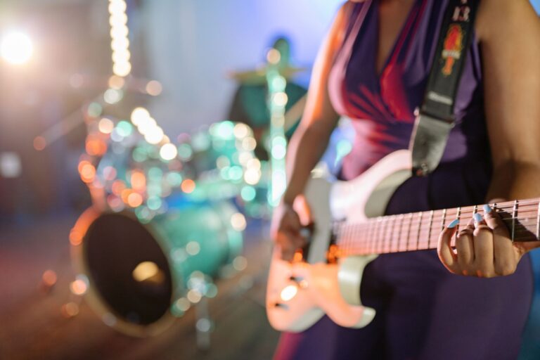 Os principais gêneros musicais e o que define cada estilo Músico tocando guitarra elétrica em um palco com bateria ao fundo e luzes coloridas de show