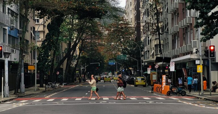 Cruzamento de rua em Florianópolis com pedestres atravessando, árvores ao redor e sinalização visível.